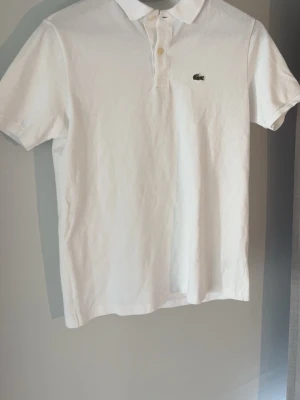 Vit Lacoste piké  - Säljer en snygg vit Lacoste piké i size XS/16 (barn size). Pikén är i super bra skick och är inte mycket använd. Skriv angående frågor eller pris.