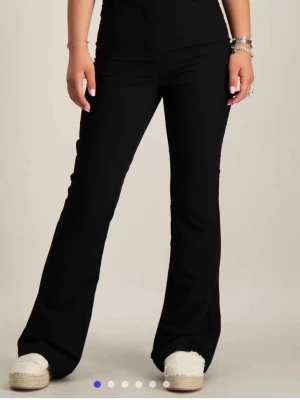 Svarta bootcut-byxor från RYVLS köpta från kidsbrandstore - Snygga svarta bootcut-byxor från RYVLS med hög midja och utsvängda ben. Byxorna har en stilren design utan synliga detaljer. De är tillverkade i ett ganska stretchigt material som ger en bekväm passform och har även en justerbar midja. Perfekta för dig som vill ha en modern och trendig look. 