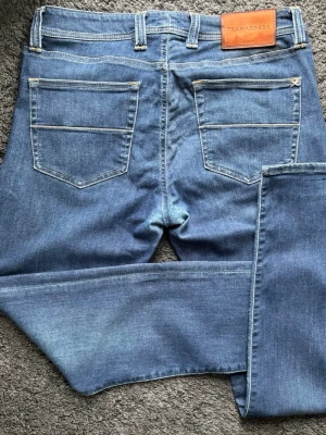 Blå jeans från Tramarossa -  Tramarossa, “Michelangelo Zip SS”-modellen. Perfekt tvätt och komfort med lyxiga detaljer. 🧵 Märke & Modell: Tramarossa – Michelangelo Zip SS 📏 Storlek & Passform: 33, slim-straight. 🧩 Material: Premium denim, 91% bomull / 5% polyester / 4% elastan 📐 Mått: Midja 45 cm, innerben 84 cm, ytterben 112 cm ✅ Skick: 7/10, fint skick, patchen har färgat av sig lite på insidan vid tvätt men inget som syns vid användning, denimet vid grenen är oxå lite tunnare  💰 Nypris ca 4000 kr ‼️Skickas inom 24h‼️