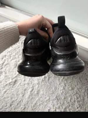 Nike Air Max 270 svarta sneakers - Säljer ett par svarta Nike Air Max 270 sneakers med mesh-överdel och synlig Air Max-dämpning i hälen. Skorna har klassisk Nike-logga på sidan och 270-märkning. De har snörning och en sportig design med låg profil.
