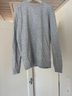 Grå sweatshirt från Dressmann - En enkel och stilren grå sweatshirt från Dressmann i storlek M med rund hals och diskret V-detalj vid halsen. Tröjan har långa ärmar och muddar vid ärmslut och nederkant. Perfekt för en avslappnad look. Priset går att diskutera!