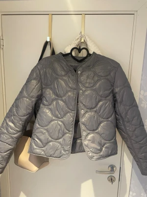 Populära jackan från Mango❣️ - Jackan är endast använd ett fåtal gånger.🤗 Tror den är i storlek xs/s. Snygg grå vindjacka med quiltat mönster och tryckknappar framtill. Jackan har en rak, boxig passform och är tillverkad i ett glansigt material som ger en modern look. Perfekt för lager-på-lager och funkar till många olika stilar.