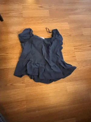 Mörkblå volangblus - Söt mörkblå blus med volangdetaljer och korta ärmar. Perfekt för dig som gillar en feminin och luftig stil. Blusen har en lös passform och rund halsringning.