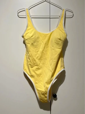 Gul baddräkt med vita kanter H&M - Snygg gul baddräkt från H&M med vita kanter. Klassisk modell med rundad halsringning och hög skärning vid benen. Materialet är stretchigt och bekvämt, perfekt för stranden eller poolen. Enkel men trendig design som sticker ut.