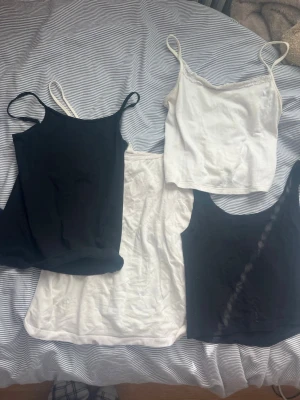 Svarta och vita linnetoppar i bomull - Fyra enkla linnetoppar i svart och vitt med smala axelband. En av de vita topparna har spetsdetalj vid urringningen. Lite olika storlekar .