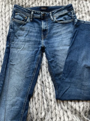 Blå jeans från Jack & Jones - Säljer ett par klassiska blå jeans från Jack & Jones med fem fickor och snygga slitningar. Jeansen har en rak passform och är gjorda i denim med en cool tvättad look. Perfekta för dig som gillar en avslappnad stil.