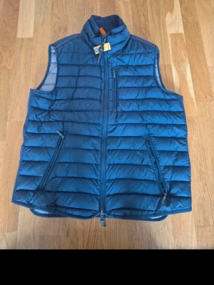 Blå dunväst från parajumpers - Snygg blå dunväst från parajumpers med quiltad design och dragkedja framtill. Västen har två snedställda fickor med dragkedja och en bröstficka. Super lightweight-material och orange detalj vid kragen. Perfekt för lager-på-lager och chill stil.