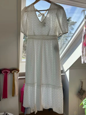 Vit långklänning med puffärmar och knyt -  Vit långklänning med blommigt mönster, puffärmar och v-ringning med knyt i ryggen. Klänningen har en volang nertill. Från Vero Moda. Ingen prislapp kvar, men aldrig använts. Pris kan diskuteras! 