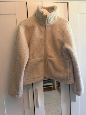 Beige teddyjacka  - Mysig beige teddyjacka med dragkedja framtill. Jackan har två stora fickor och är gjord i fluffigt teddy-material som ger en avslappnad och trendig look. Perfekt för kyliga dagar när du vill vara både varm och snygg.