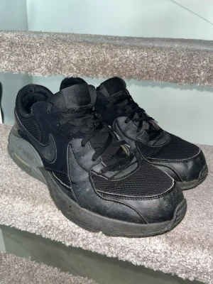 Nike Air Max svarta sneakers - Svarta Nike Air Max sneakers med mesh och läderdetaljer. Klassisk swoosh på sidan, tjock sula med synlig Air-enhet och lågt skaft. Skorna har svarta skosnören och en sportig vibe som passar till streetwear.