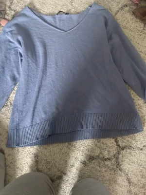 Blå stickad tröja med v-ringning - Säljer en snygg blå stickad tröja med v-ringad hals och långa ärmar. Tröjan har bred ribbstickad kant nedtill som ger en cool detalj. Perfekt att matcha med jeans eller kjol för en avslappnad look.