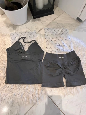 Stone DFYNE - Säljer ett grått träningsset från DFYNE som består av en sportig crop top med smala axelband och matchande shorts med hög midja. Materialet är stretchigt och designen är figurnära, perfekt för gym eller träning. Impact 4.5