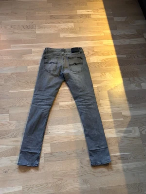 Grå slim fit jeans från Nudie jeans - Säljer ett par grå jeans från nudie jeans med klassisk femficksmodell och diskreta slitningar framtill. Jeansen har normal midja, dragkedjegylf och är tillverkade i stretchigt denim för extra komfort. Modellen på jeansen är lean Dean. Om du har några frågar är det bara att höra av sig!