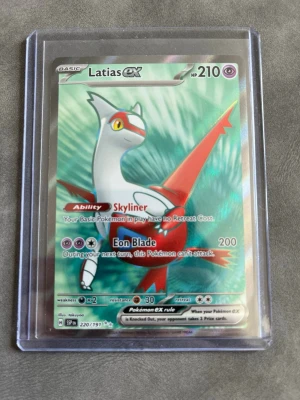 Latias EX Pokémonkort - Latias EX holografiskt Pokémonkort med 210 HP och attacken Eon Blade. Kortet har färger i vitt, rött och grönt och ligger i ett genomskinligt plastskydd. Perfekt för samlare eller Pokémonfans.