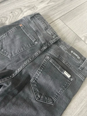 Mörkgrå bootcut jeans från GARCIA  - Snygga mörkgrå jeans från Garcia med klassisk femficksmodell och bootcut passform med en gråsvart färg. Jeansen har normal midja och stängs med knapp och dragkedja. Perfekta för dig som gillar en retroinspirerad look.