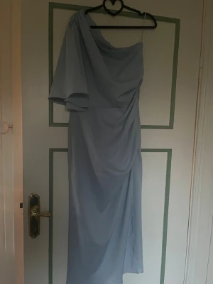Ljusblå långklänning från Bubbleroom - Säljer en elegant ljusblå långklänning från Bubbleroom med oneshoulder-design och draperad detalj. Klänningen har ett luftigt fall och är perfekt för dig som vill sticka ut med en unik look. Materialet känns mjukt och bekvämt mot huden.