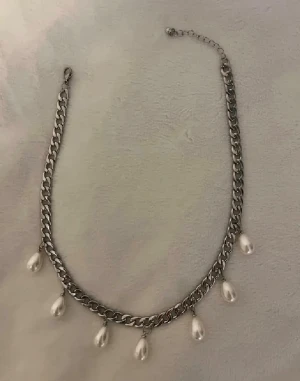 Kedjehalsband med pärldroppe - Snyggt halsband med grov silverfärgad kedja och en vit pärldroppe som hänge. Justerbar längd med förlängningskedja. Perfekt för att ge din outfit en cool touch.