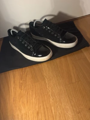 Svarta sneakers från Lanvin - Snygga svarta sneakers från Lanvin med glansig tå och detaljer i mocka. Skorna har vita sulor och klassisk snörning. Perfekta för dig som vill ha en stilren och trendig look.