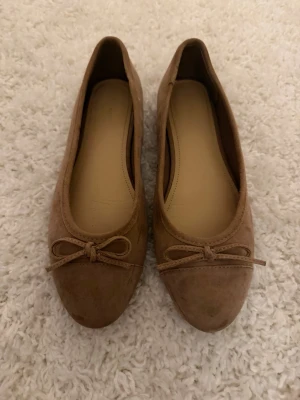 Beige ballerinaskor med rosett - Snygga ballerinaskor i beige mockaimitation med rund tå och liten rosett framtill. Storlek 39💓