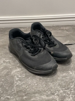 Svarta Nike sneakers med mesh - Säljer ett par svarta Nike sneakers med låg profil och klassisk design. Skorna har meshmaterial på ovansidan för bra ventilation och gummisula med mönster för extra grepp. Perfekt för dig som gillar sportig stil och komfort.