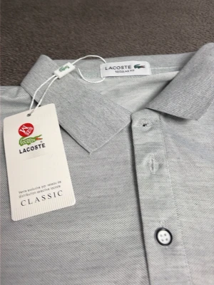 Ljusgrå pikétröja från Lacoste M - Snygg ljusgrå pikétröja från Lacoste med klassisk krage och knappslå framtill. Tröjan har korta ärmar och den ikoniska gröna krokodilloggan på bröstet. Tillverkad i mjuk bomull för en bekväm känsla.
