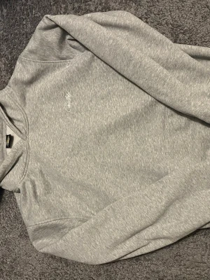 Grå hoodie från cortez - Snygg grå hoodie från cortez med diskret broderad logga på bröstet. Tillverkad i mjukt och bekvämt material, har klassisk huva och magficka. Perfekt för chill dagar.
