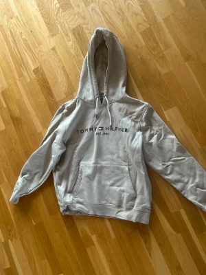 Beige hoodie från Tommy Hilfiger - Snygg beige hoodie från Tommy Hilfiger med text över bröstet. Köpte den för ett tag sen men har inte blivit använd särskilt mycket