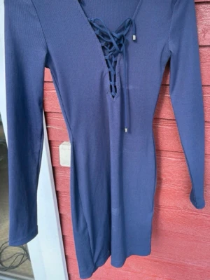 Marinblå ribbad klänning Gina Tricot - Snygg marinblå ribbad klänning från Gina Tricot i kort modell. Klänningen har lång ärm, v-ringning med snörning framtill och är tillverkad i ett stretchigt material som sitter snyggt på kroppen. Perfekt för dig som gillar enkel men trendig stil.