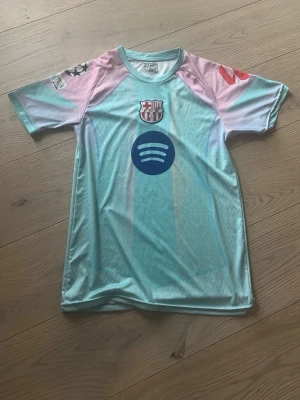 Barcelona matchtröja Lamine Yamal - Snygg Barcelona matchtröja i ljusblått med rosa ärmar, officiella klubbmärket och sponsorlogga på bröstet. Nummer 10 och Lamine Yamal på ryggen. Tillverkad i lätt och ventilerande funktionsmaterial, perfekt för fotbollsträning eller match,så att ni vet är den slim fit 