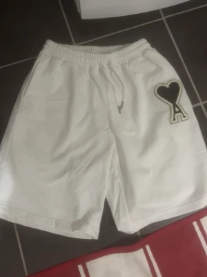 Vita shorts med hjärtdetalj - Säljer ett par vita ami Paris shorts med elastisk midja och snörning. Perfekta för sommaren och riktigt sköna att bära till vardags. Materialet känns mjukt och luftigt.