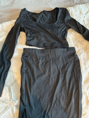 Svart ribbad kjol och långarmad tröja  - Säljer en svart, ribbad kjol och långarmad tröja med kroppsnära passform och hög midja. Kjolen har en enkel och stilren design som passar till många olika looks. Materialet är stretchigt och bekvämt, perfekt för dig som gillar en tight siluett. 