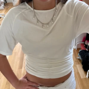 Vit croppad topp med tajtare midja - Säljer en vit croppad topp med korta ärmar och snygg tajtare midja. Toppen har en tight passform och är perfekt till höga jeans eller kjol. Enkel och stilren design som passar till många olika looks.