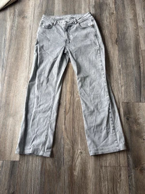 Grå raka jeans som är mid waist - Säljer ett par grå jeans med raka ben som är mid waist. Klassisk femficksmodell med bälteshällor och knappgylf. Jeansen har en stilren look och passar perfekt till en avslappnad outfit. Materialet är denim i bomull. Uppsydda och passar dig som är 165