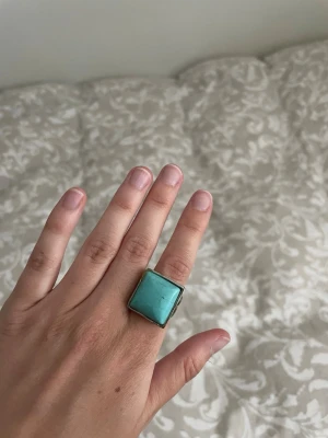 Stor silverring med turkos sten - Säljer en statementring i silverfärgad metall med en stor fyrkantig turkos sten. Ringen har en bred ringbas och den turkosa stenen har naturliga ådringar som ger en unik look. 