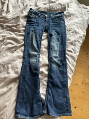 Blå bootcut jeans från Cheap Monday - Säljer ett par blå bootcut jeans från Cheap Monday i modell booty bei med klassisk femficksmodell och coolt grönt märke bak i midjan. Jeansen har slitningar framtill och är tillverkade i mjuk denim med lätt stretch. Perfekta för en avslappnad och trendig look. har sytt om så de blir mer low waisted och mindre i storlek typ 26- eller 25/30 ❤️