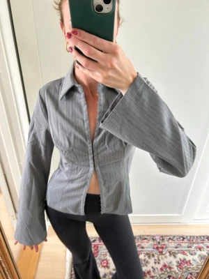 Grå randig skjorta med vida ärmar - Säljer denna as snygga skjort topp med vida ärmar och justerbar knytning!! Köpt i New York och aldrig använd 🩷nypris 500kr