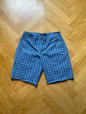 Blårutiga shorts  - Snygga blårutiga shorts  med klassisk passform. Shortsen har fickor fram och bak, bälteshällor och stängs med knapp och dragkedja. Perfekta för sommardagar och har en avslappnad men stilren look.