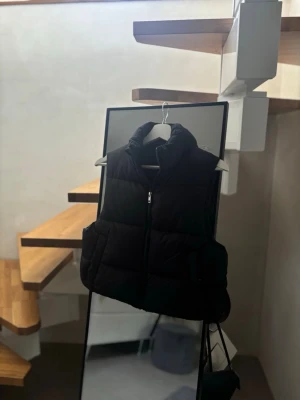 Svart dunväst med hög krage - Svart dunväst med hög krage och dragkedja framtill. 