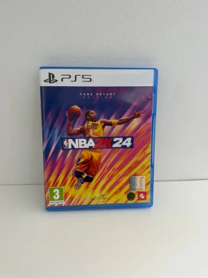 NBA 2K24 Kobe Bryant Edition PS5 - NBA 2K24 Kobe Bryant Edition till PS5 med färgstark omslagsdesign och bonuskod för förhandsbokning. Spelet kommer i ett blått plastfodral och innehåller skiva samt bonusmaterial. Perfekt för basketfans som vill spela som legender på PlayStation 5. Använd men i mycket gott skick