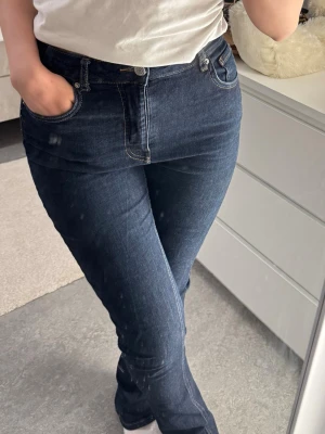 Mörkblå raka jeans med hög midja - Snygga mörkblå jeans med raka ben och hög midja. Klassisk femficksmodell med kontrastsömmar och knappgylf. Jeansen har en tidlös look och passar perfekt till en enkel t-shirt eller hoodie. Materialet är denim i bomull med lite stretch för extra komfort.