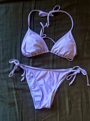 Ljuslila bikini med knyt - Endast testad! Snygg ljuslila bikini med trekantsöverdel och knyt både i nacken och ryggen. Underdelen har knyt i sidorna för justerbar passform. Perfekt för sommaren! Skriv och fråga vid fundering/mer bilder! 