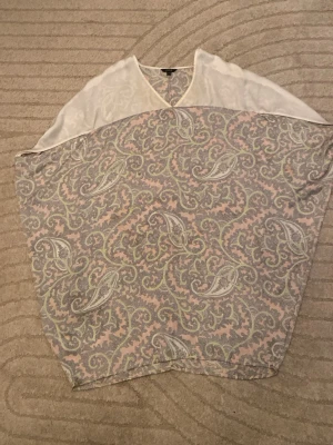 Pastellmönstrad blus med paisley - Säljer en stor, tunn blus i pastellfärger med paisleymönster i ljusrosa, grått och vitt. Blusen har en mjuk, flowy känsla och V-formad halsringning. Perfekt för sommarkvällar
