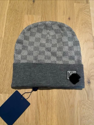 Grå mössa - Snygg grå mössa med diskret rutmönster och vikt kant. på sidan ger en exklusiv touch. Tillverkad i mjukt stickat material som håller dig varm och stilren under kalla dagar.