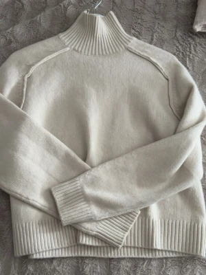 Vit stickad polotröja - Säljer en stilren vit stickad polotröja med ribbade muddar och hög krage. Tröjan har långärmad design och är gjord i mjukt material som passar perfekt för kyliga dagar. Enkel och klassisk modell som är lätt att matcha med olika outfits.Är i storlek Xs ifrån hm 