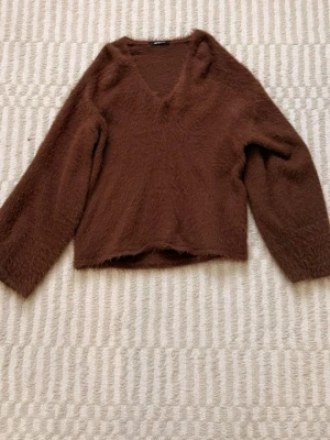 Brun fluffig stickad tröja Gina Tricot - Mysig brun stickad tröja från Gina Tricot med fluffig textur och V-ringning. Tröjan har långa och luftiga ärmar och en avslappnad passform. Materialet känns mjukt och ger en trendig look. Storlek S, men passar mig som brukar ha M