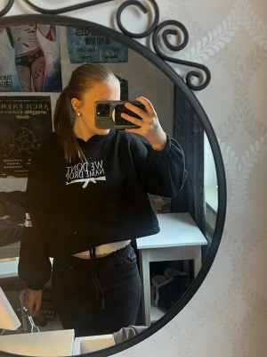 Svart cropped hoodie We Don’t Name Drop - Säljer en svart cropped hoodie från ”wash cold inside out do not trumble  dry”med vit text och gevärsgrafik på bröstet. Hoodien har huva och dragsko i nederkanten. Perfekt för en edgy streetwear-look och passar till både jeans och kjol.