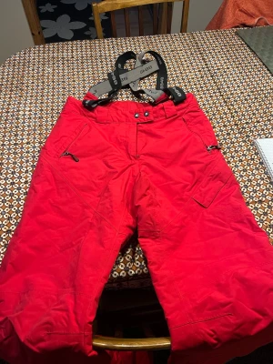 Röda täckbyxor från 8848 Altitude - Snygga röda täckbyxor från 8848 Altitude med justerbara hängslen och dragkedjefickor. Perfekta för vinterns alla äventyr. Byxorna har en bekväm passform och slitstarkt material som står emot kyla och snö. Pris kan sänkas vid snabb affär 🤝