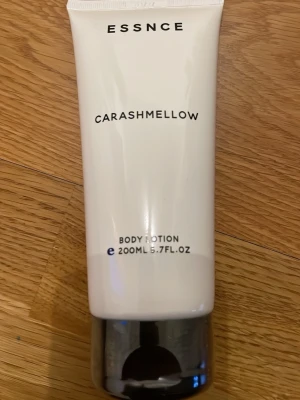 Essnce Carashmellow Body Lotion oöppnad - Body lotion från Essnce i doften Carashmellow med toner av karamell, mjölk och vanilj. Tuben är vit med svart lock och rymmer 200 ml. Tillverkad i Frankrike och innehåller inga råvaror av animaliskt ursprung. Plasten sitter Fof på så helt oöppnad