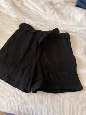 Svarta shorts med knytband - Avslappnande svarta tygshorts från Gekås. Knytband i midjan som gör att de kan justeras. Aldrig använda, endast testade. Ingen prislapp tyvärr. 