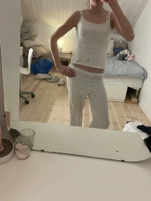 Vit pyjamas med spetsdetaljer - Mysig vit pyjamas med linne och långa byxor. Linnet har smala axelband och spetsdetaljer vid axlarna. Byxorna är randiga i vitt och ljusgrått med rak passform. Perfekt för chillkvällar hemma.❤️